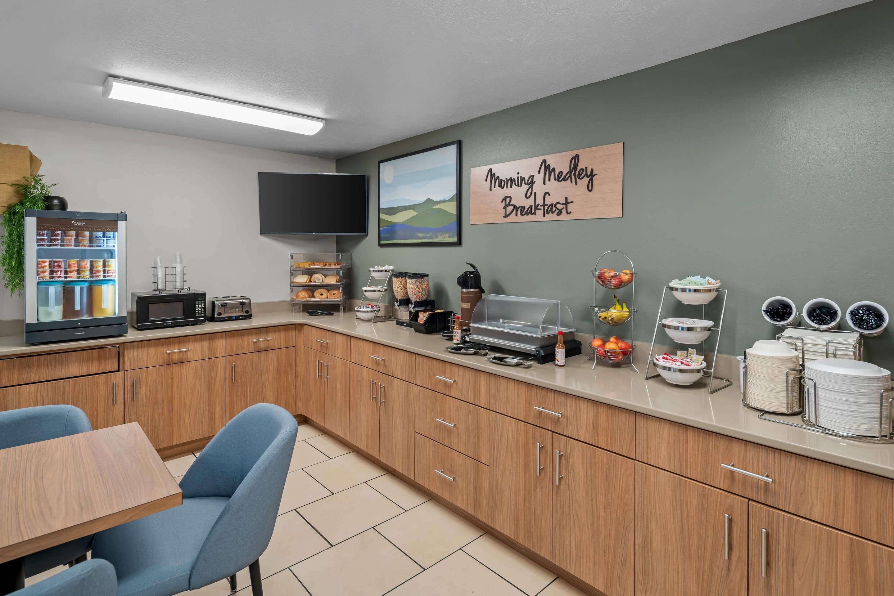 A breakfast area with a refrigerator, microwave, toaster, and a sign that reads 'Morning Medley Breakfast.'