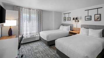Une chambre d’hôtel avec deux lits, un bureau, une télévision, un radiateur et des tableaux encadrés au mur.