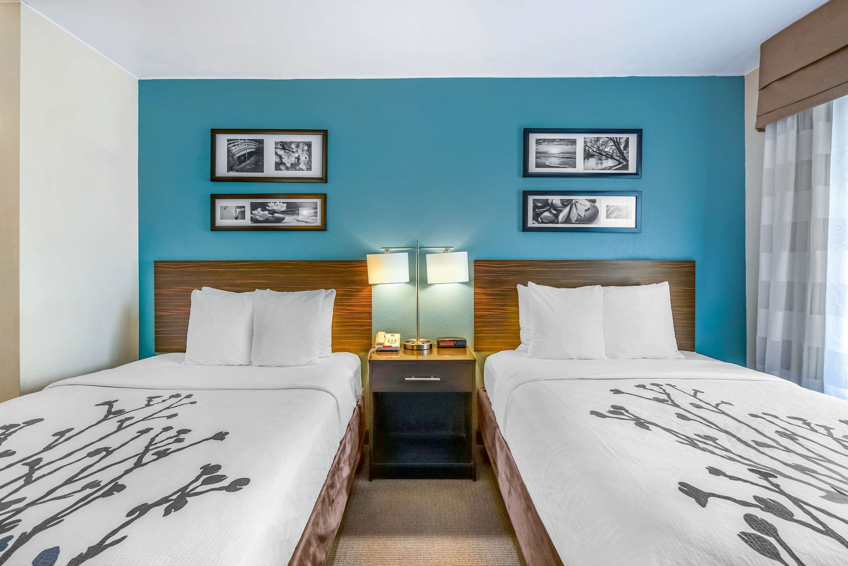 A hotel room with two beds, a nightstand with a lamp, and framed pictures on the wall.