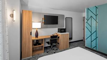 A hotel room with a bed, a desk with a chair, a TV, a microwave, and a large mirror.