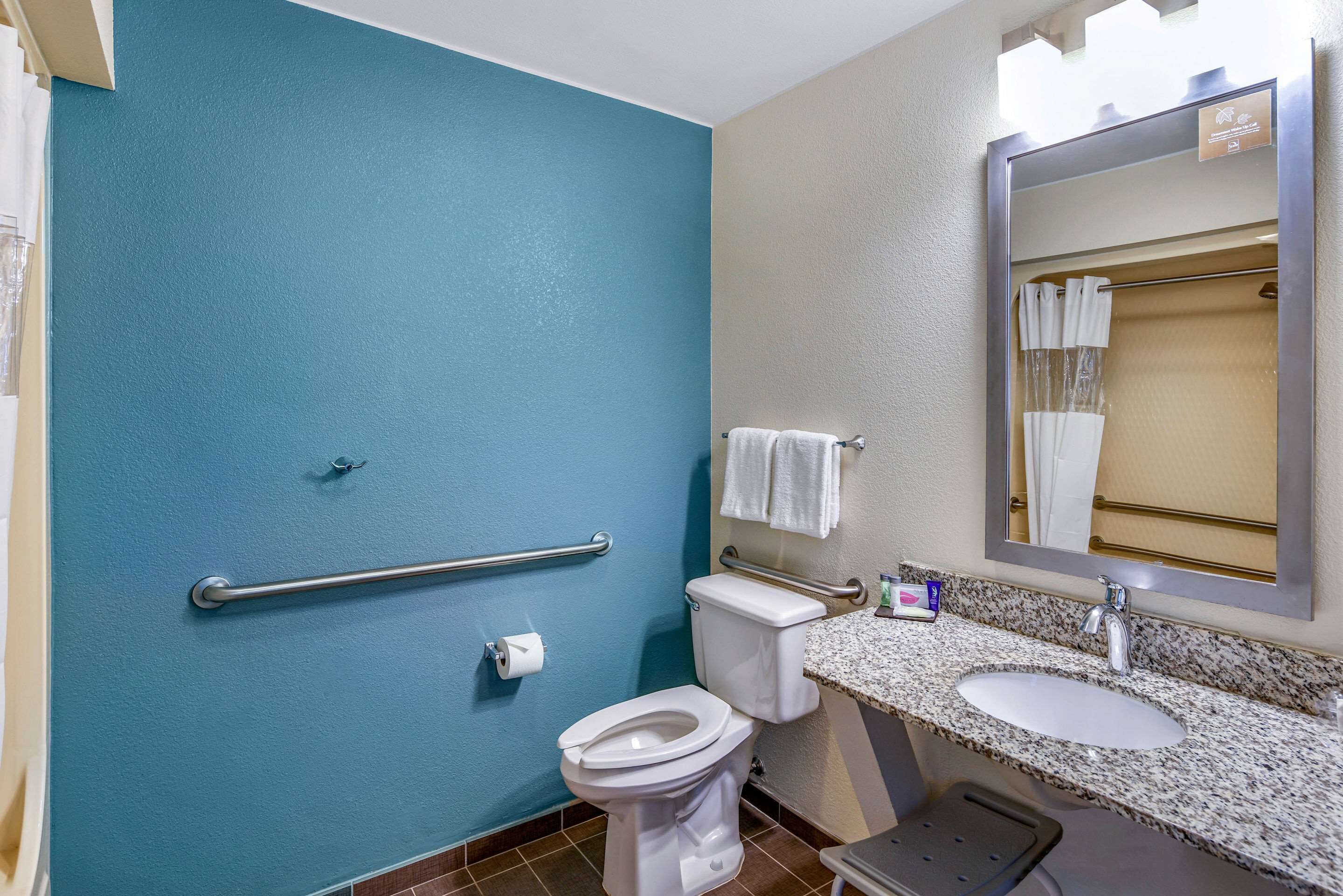 A bathroom with a blue wall, a white toilet, a sink with a mirror, and a handrail.