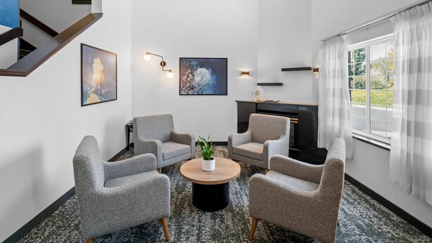 A modern living room with grey armchairs, a round coffee table, and a fireplace. - Sleep Inn near Washington State Line (Post Falls)