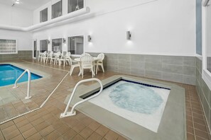 An indoor swimming pool area with a hot tub, a pool table, and a seating area with chairs.