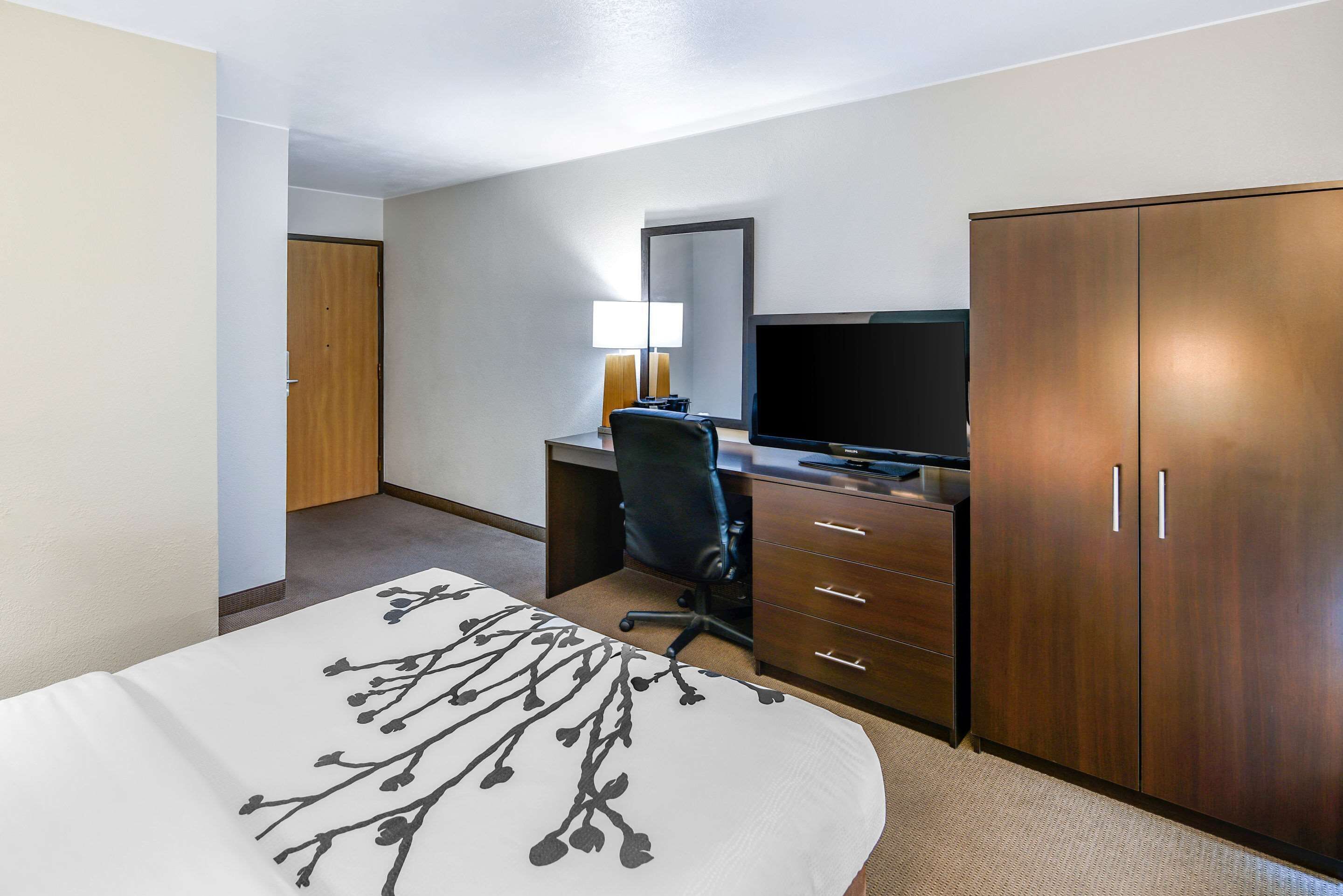 A hotel room with a bed, a desk with a TV, a chair, and a wardrobe.
