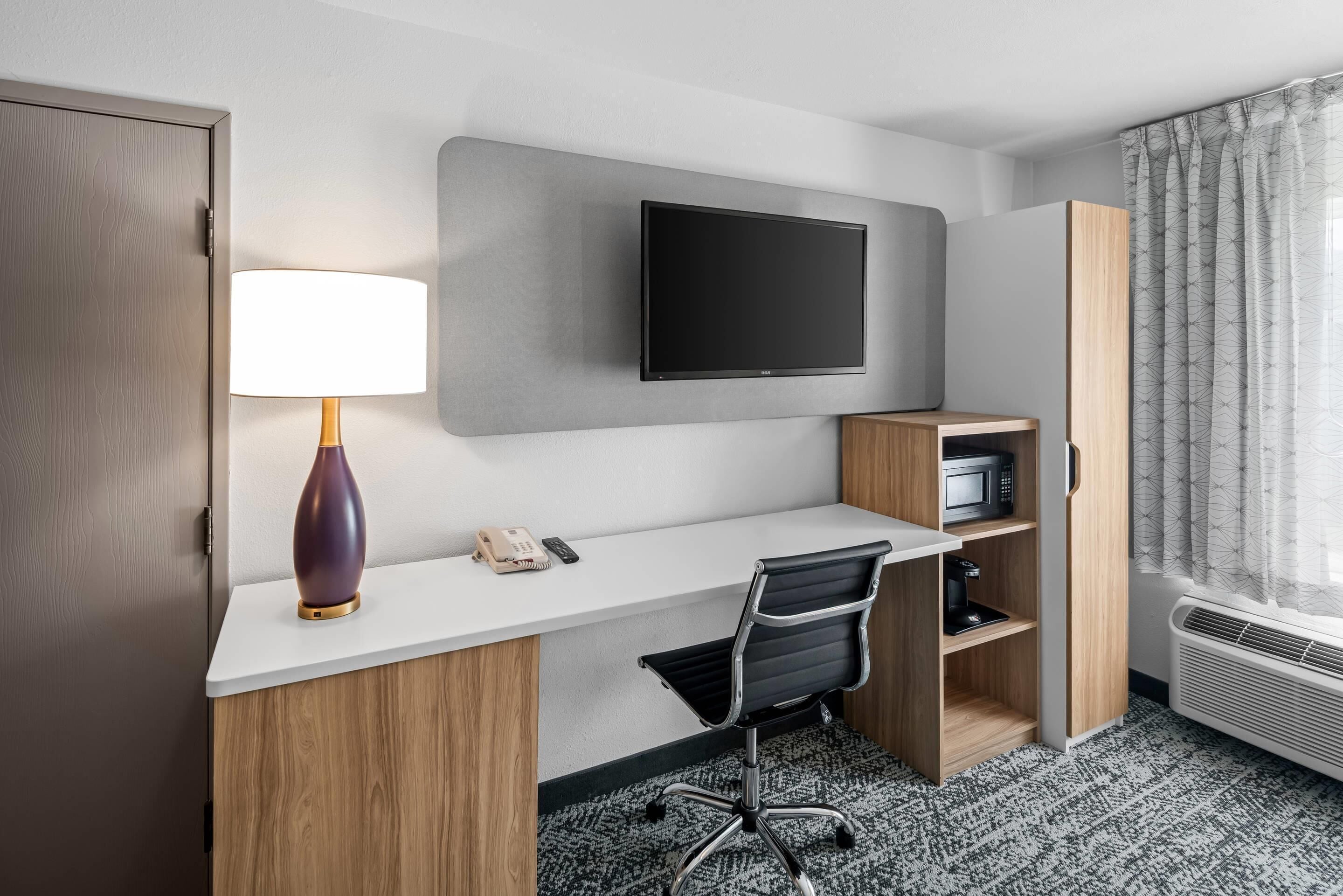 A hotel room with a desk, chair, TV, lamp, phone, microwave, and wardrobe.