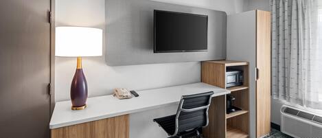 A hotel room with a desk, chair, TV, lamp, phone, microwave, and wardrobe.