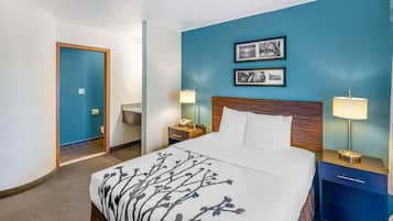 Une chambre d’hôtel avec un grand lit, deux tables de chevet, une petite table, une tête de lit en bois et deux tableaux encadrés accrochés au mur.