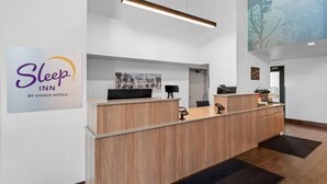 A reception desk with a sign for Sleep Inn by Choice Hotels, a computer, a telephone, and a small desk lamp. - Sleep Inn near Washington State Line (Post Falls)
