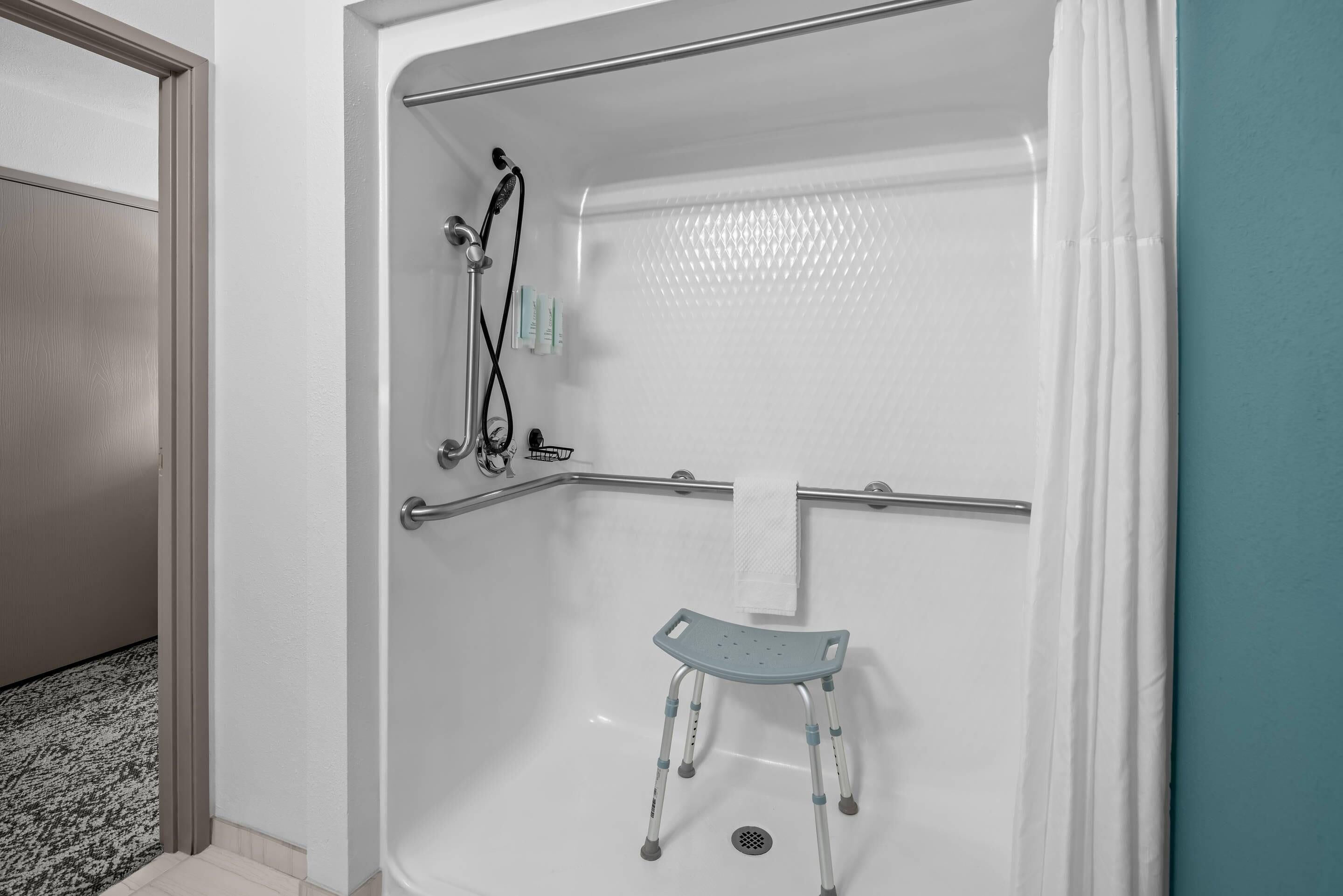 A walk-in shower with a grab bar, a shower chair, and a handheld showerhead.