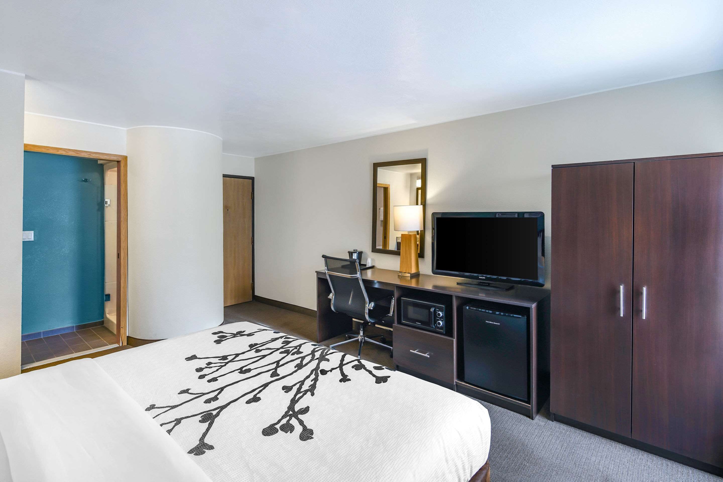 A hotel room with a bed, a desk with a computer, a television, and a wardrobe.