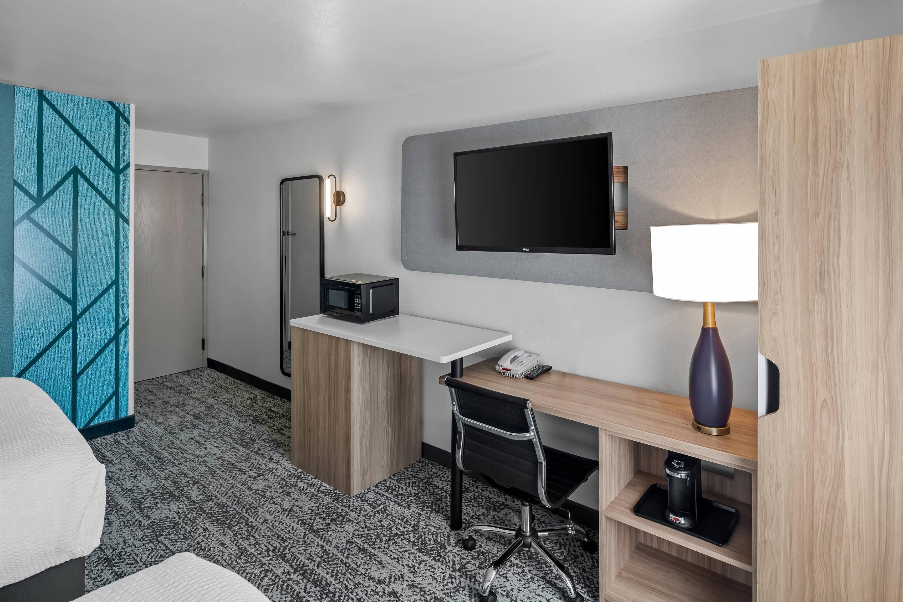 A hotel room with a desk, chair, TV, and a minibar.