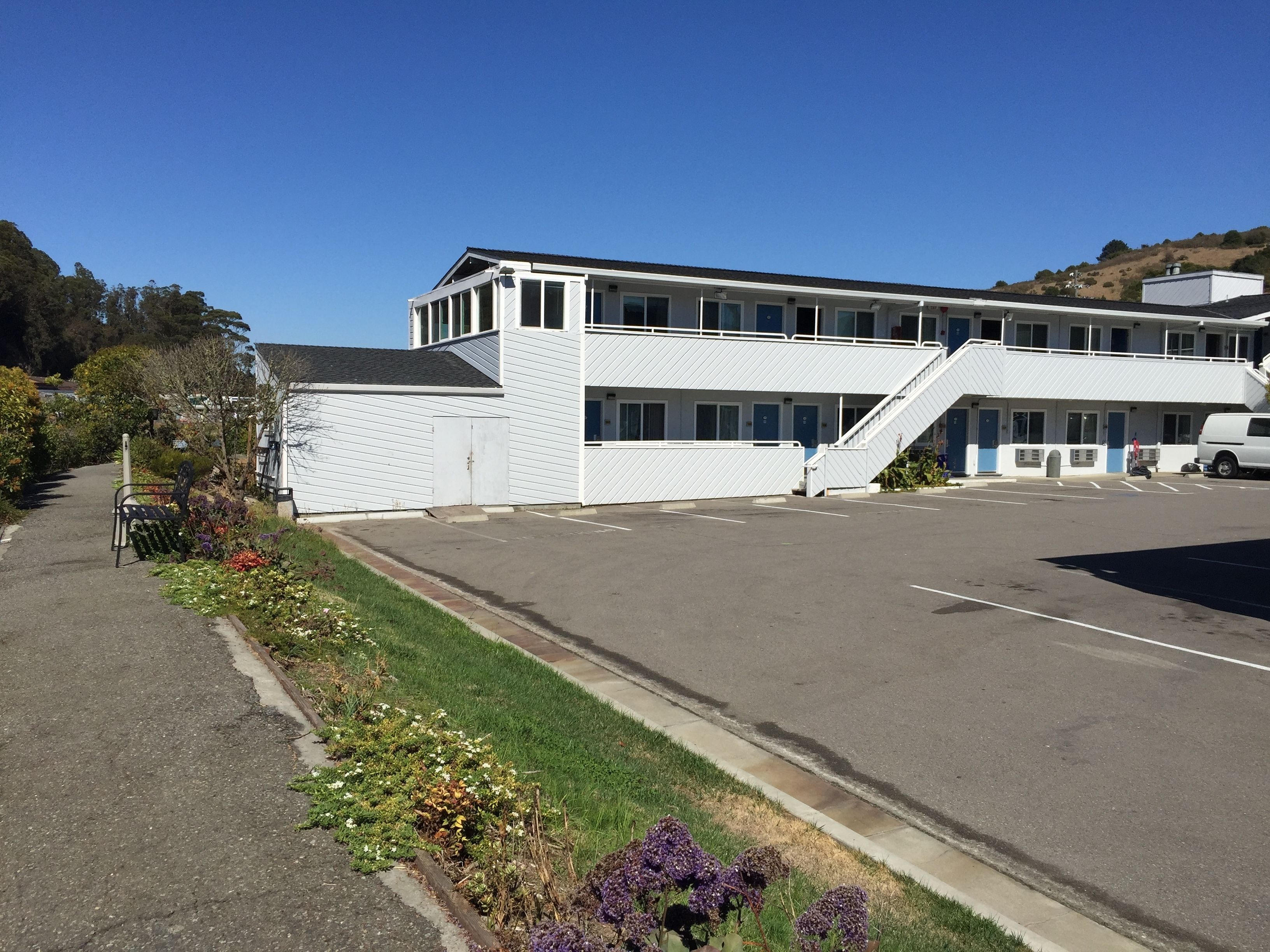 A two-story building with a parking lot, a covered walkway, and a garden area with flowers.