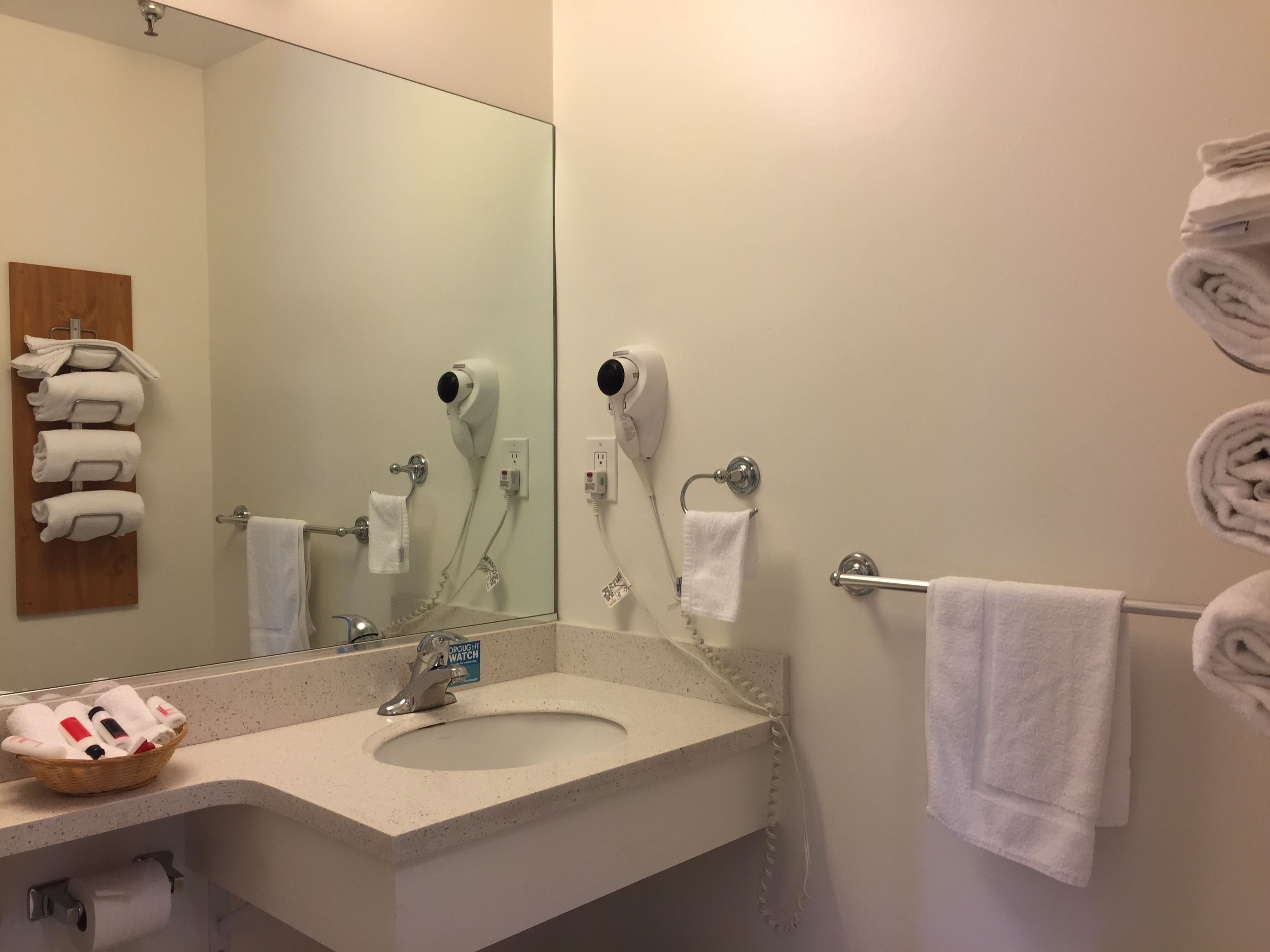 A bathroom with a sink, two hair dryers, a towel rack, and a mirror.