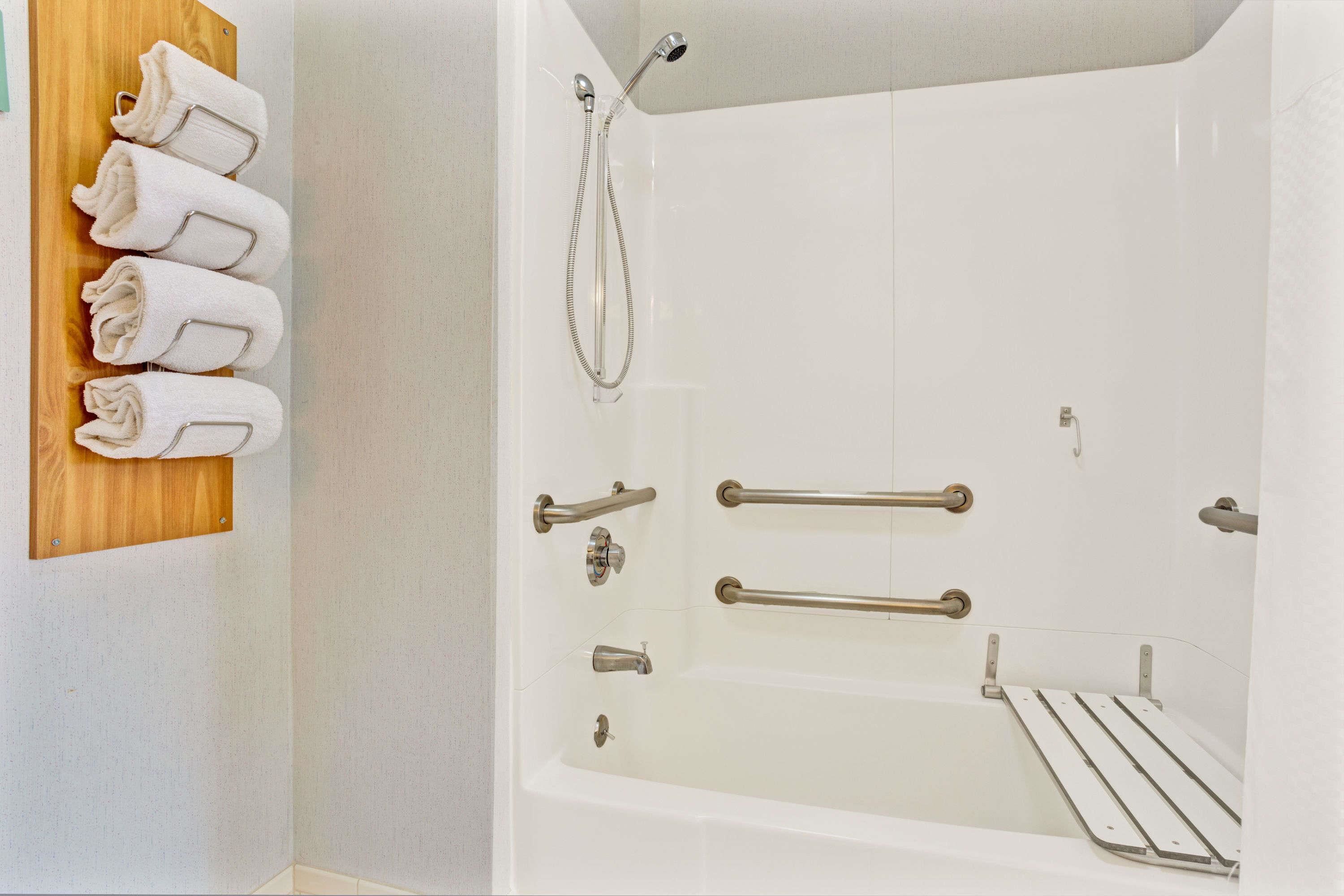 A white bathtub with grab bars, a showerhead, and a towel rack with towels.
