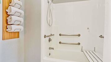 A white bathtub with grab bars, a showerhead, and a towel rack with towels.
