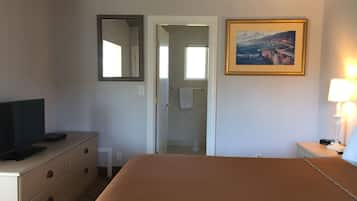 A hotel room with a bed, a television on a dresser, a painting on the wall, and a lamp on a bedside table.