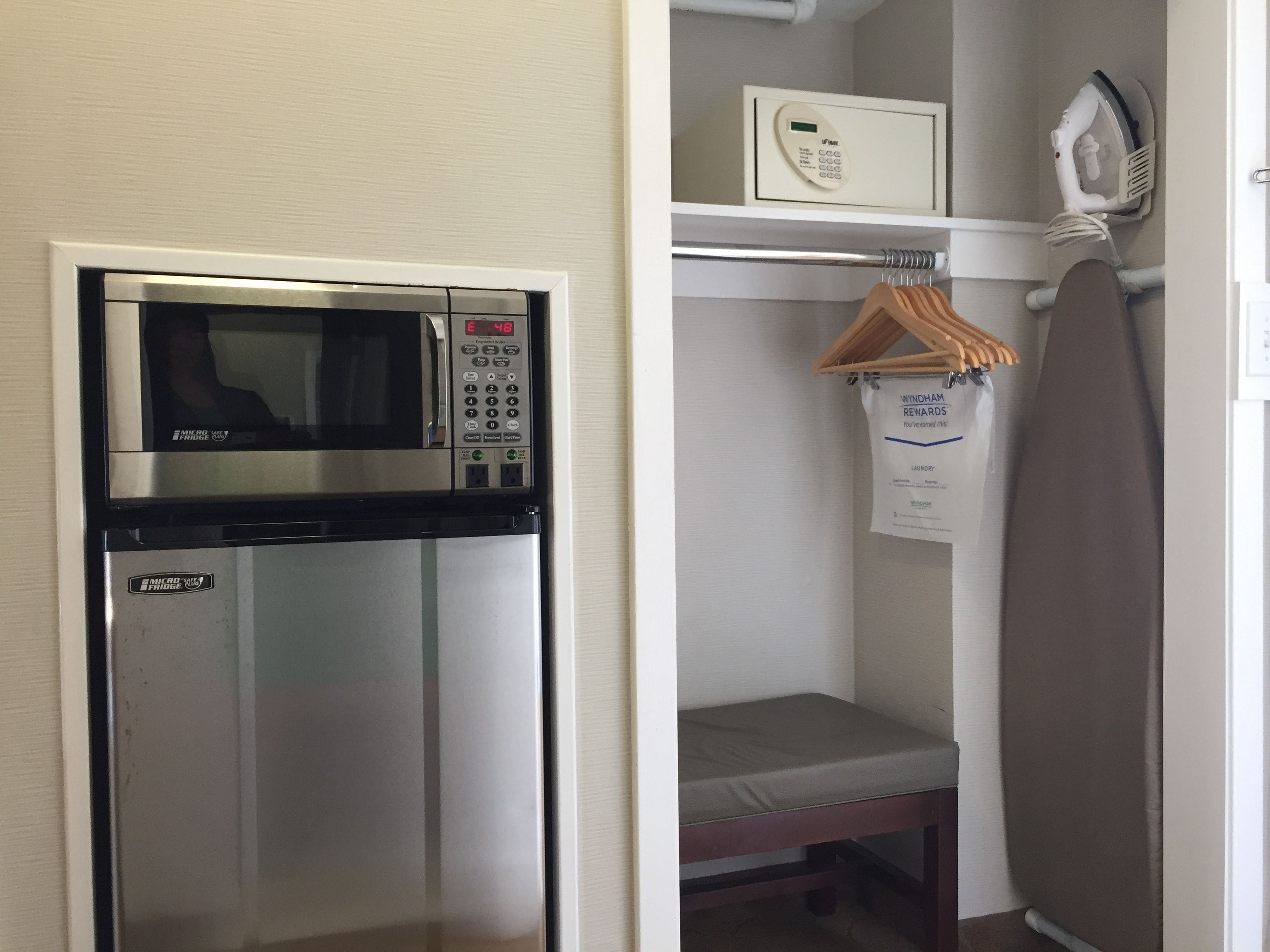 A compact kitchenette with a microwave, a mini fridge, and a hanging clothes rack.