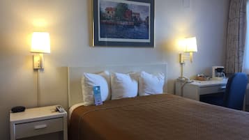 Une chambre d’hôtel comprenant un lit, deux tables de chevet, un bureau avec une chaise, un tableau au mur et deux lampes.