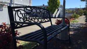A black metal bench with a decorative backrest in a sunny outdoor area with a clear sky.