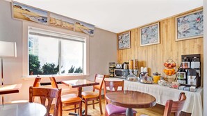 A dining area with wooden tables and chairs, a coffee station, and artwork on the walls.