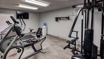 Une salle de sport équipée de machines de cardio, de matériel de musculation et d’un téléviseur fixé au mur.