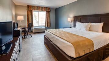 Quarto de hotel com uma cama grande, uma mesa de trabalho com televisão e uma cadeira.