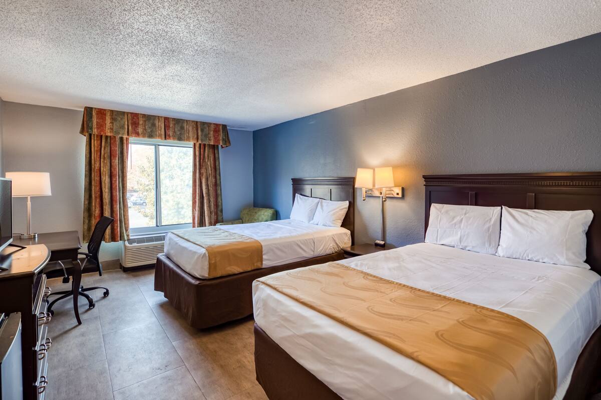 Een hotelkamer met twee bedden, een bureau, een stoel en een raam met gordijnen.