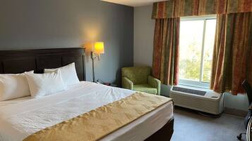 A hotel room with a large bed, a nightstand with a lamp, a green armchair, and a window with curtains.