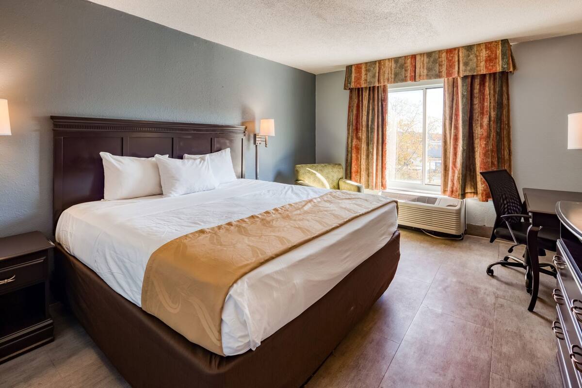 Een hotelkamer met een groot bed, een bureau, een stoel en een raam met gordijnen.