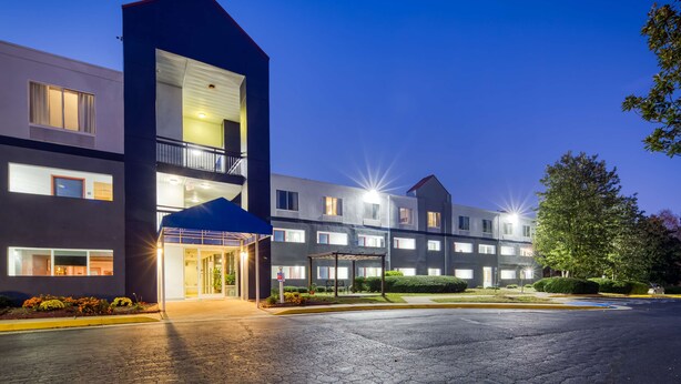 Ein modernes Hotel mit zweistöckiger Bauweise, überdachter Zufahrt und einem Parkplatz.