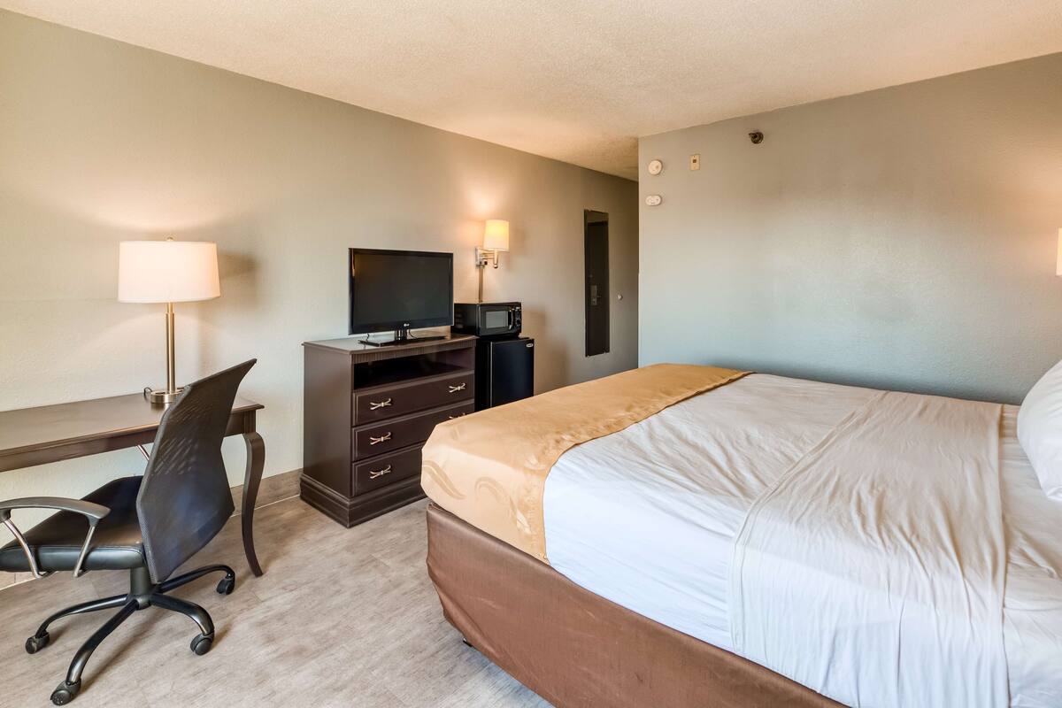 Een hotelkamer met een bed, een bureau met stoel, een televisie en een lamp.