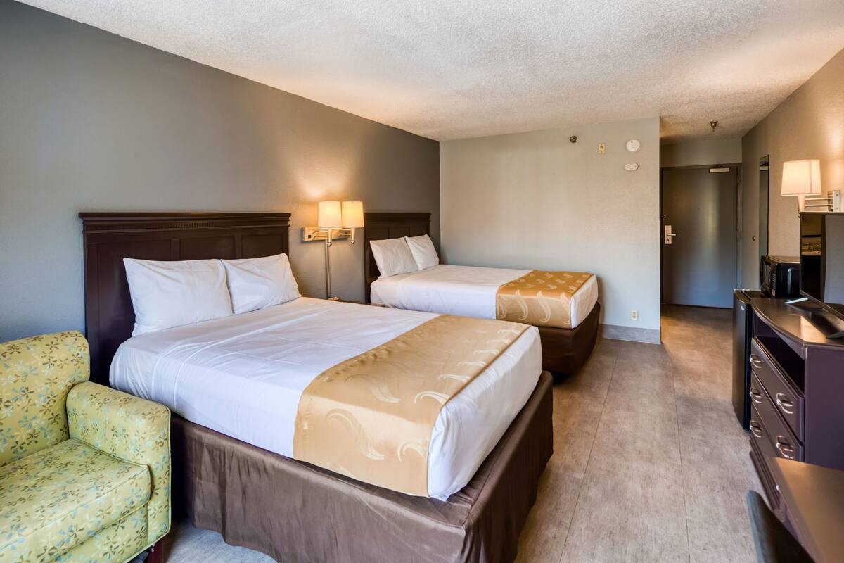 Een hotelkamer met twee bedden, een bank, een dressoir en een lamp.