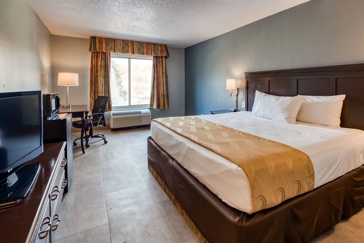Hotelkamer met een groot bed, een bureau met een televisie, een stoel, een airconditioning en een raam met gordijnen.