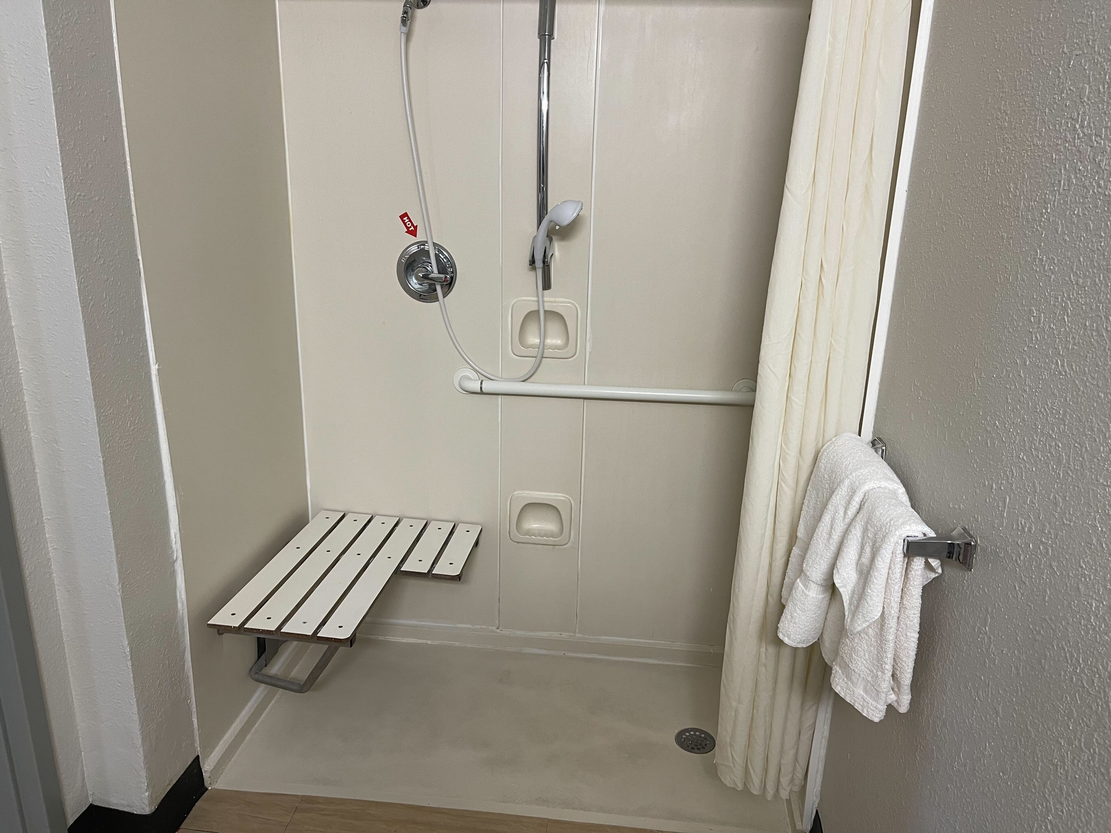 A shower area with a bench, a towel rack, and a showerhead.