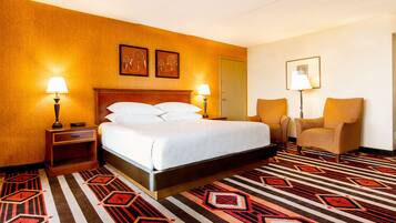 Una habitación de hotel con una cama grande, dos lámparas de noche, una silla y una alfombra estampada.