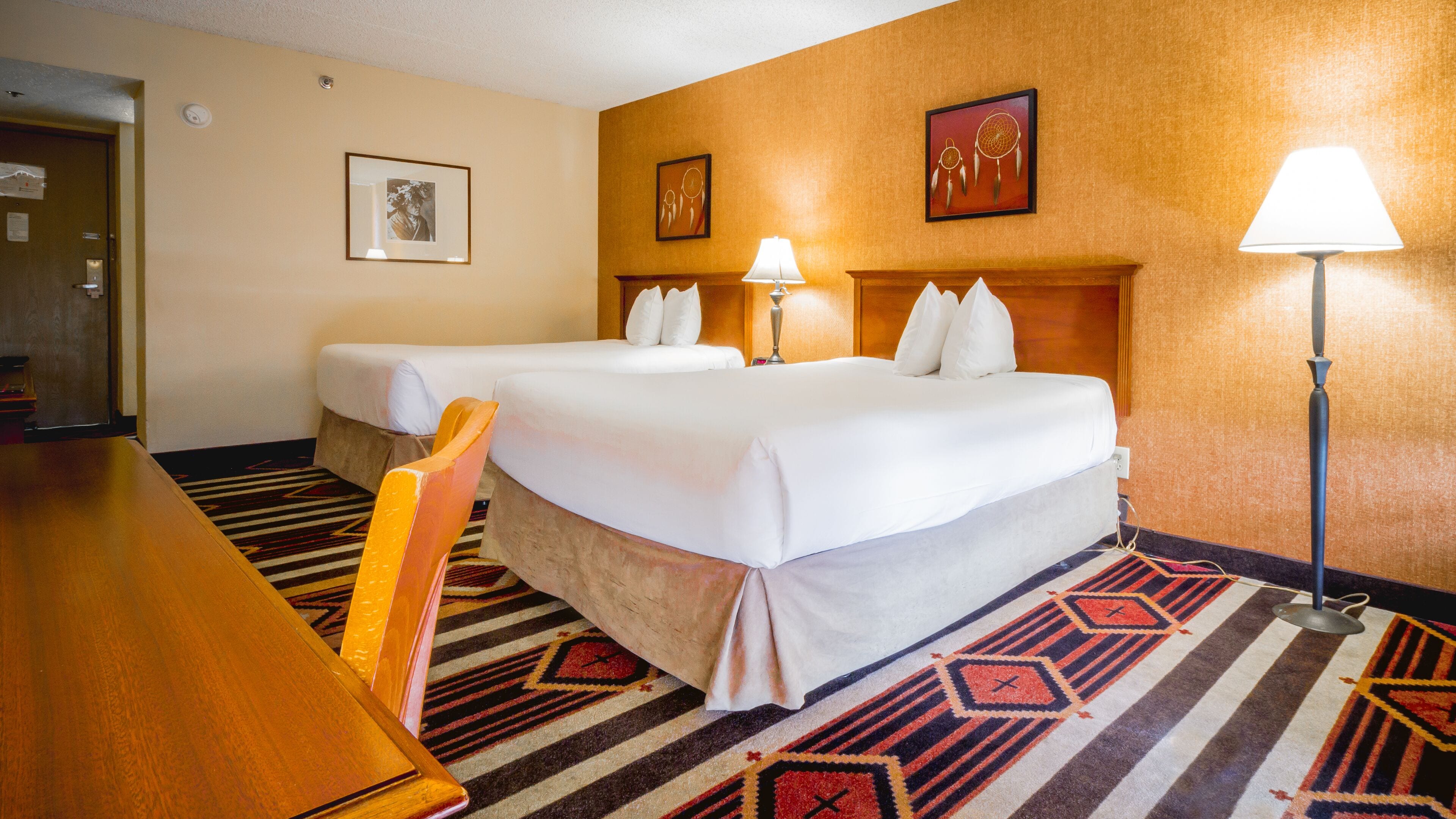 A hotel room with two beds, a desk, and a patterned carpet.