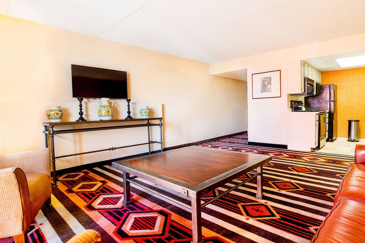 Una sala de estar con sofá, una mesa de centro, televisor y una zona de cocina con microondas y fregadero.