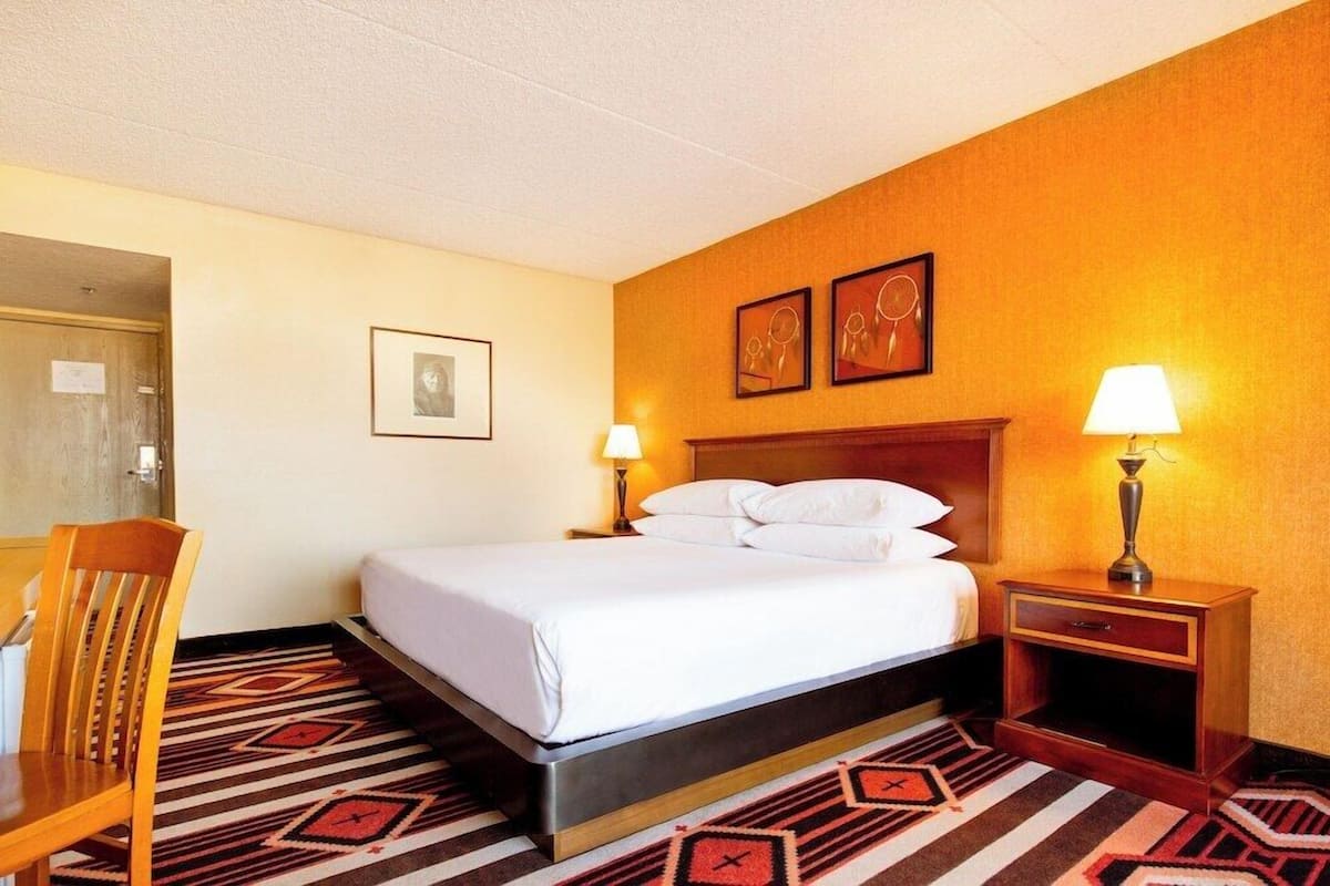 Una habitación de hotel con cama, dos mesitas de noche, una silla, un escritorio y una puerta.