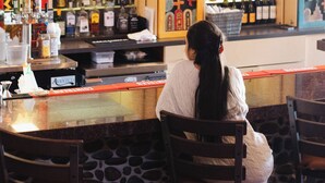 A bar with a variety of bottles and a person seated at a table. - Nativo Lodge Hotel Albuquerque (Albuquerque)