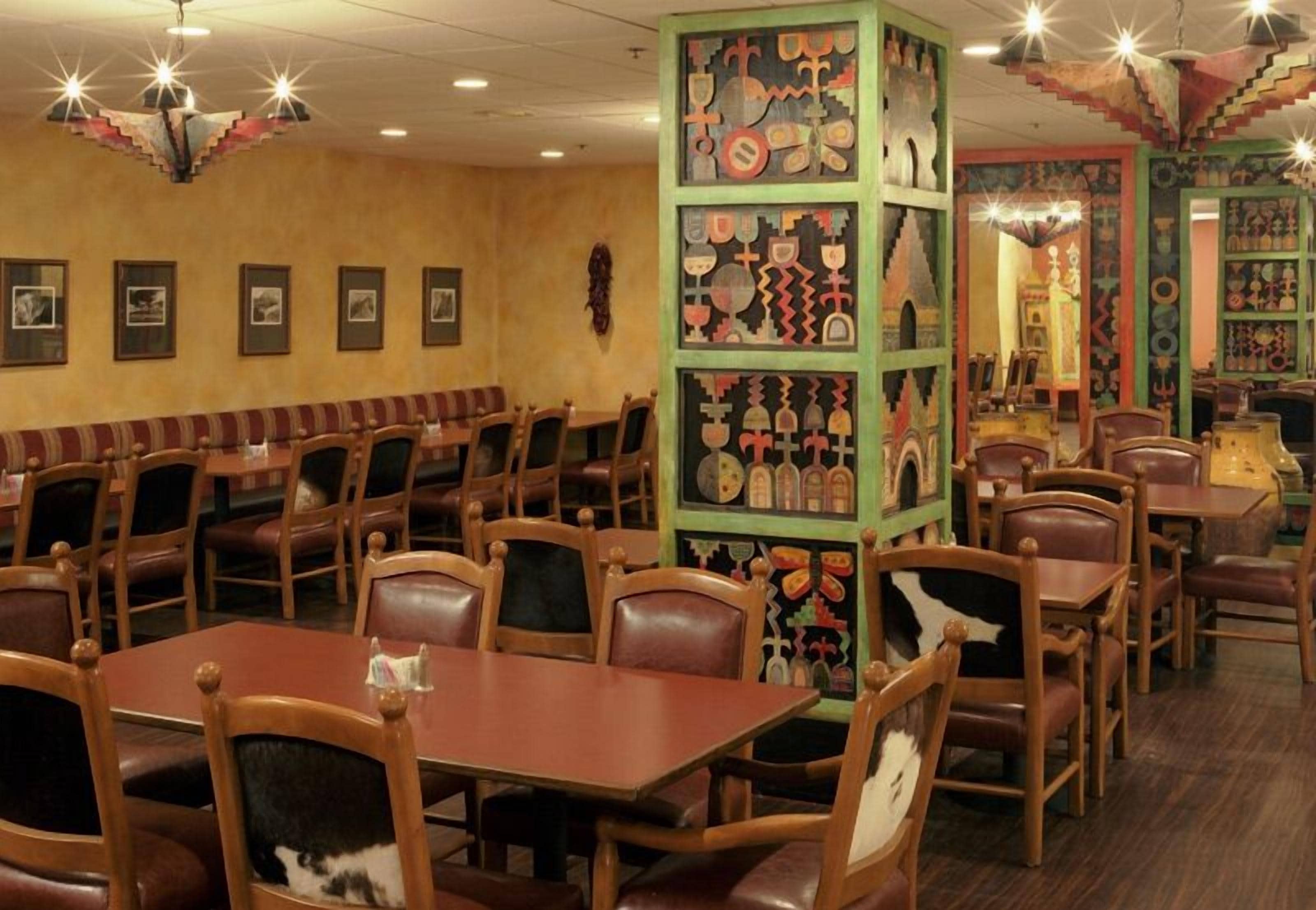 A restaurant with wooden tables and chairs, a central decorative pillar with various items, and framed pictures on the walls.