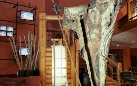 A lobby with a large sculpture, a wooden staircase, and a television screen.
