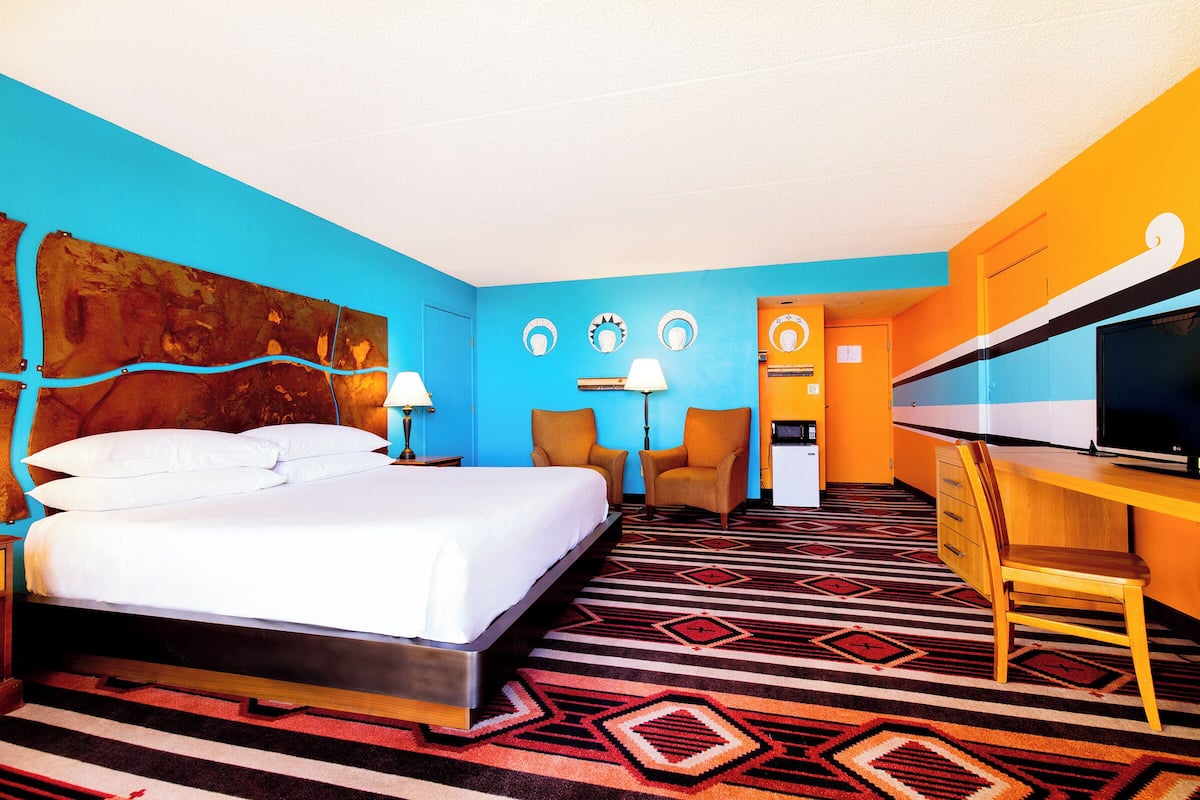 Una habitación de hotel con cama, dos sillas, escritorio con televisor y puerta de baño.