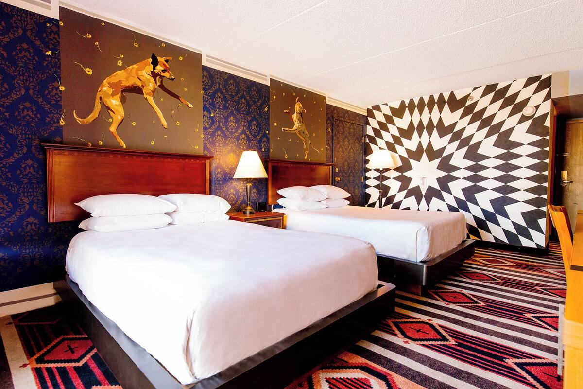 Una habitación de hotel con dos camas, alfombra estampada y diseño geométrico en la pared.