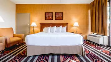 Une chambre d’hôtel avec un grand lit, deux lampes de chevet, un climatiseur fixé au mur, une moquette à motifs et une porte.
