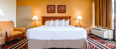 Ett hotellrum med en stor säng, två sänglampor, en väggmonterad luftkonditioneringsanläggning, en mönstrad matta och en dörr.