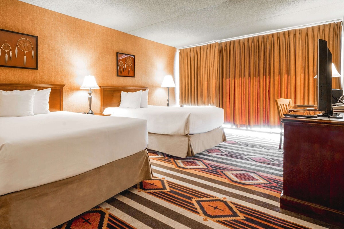 Una habitación de hotel con dos camas, un escritorio con computadora y un ventanal con cortinas.