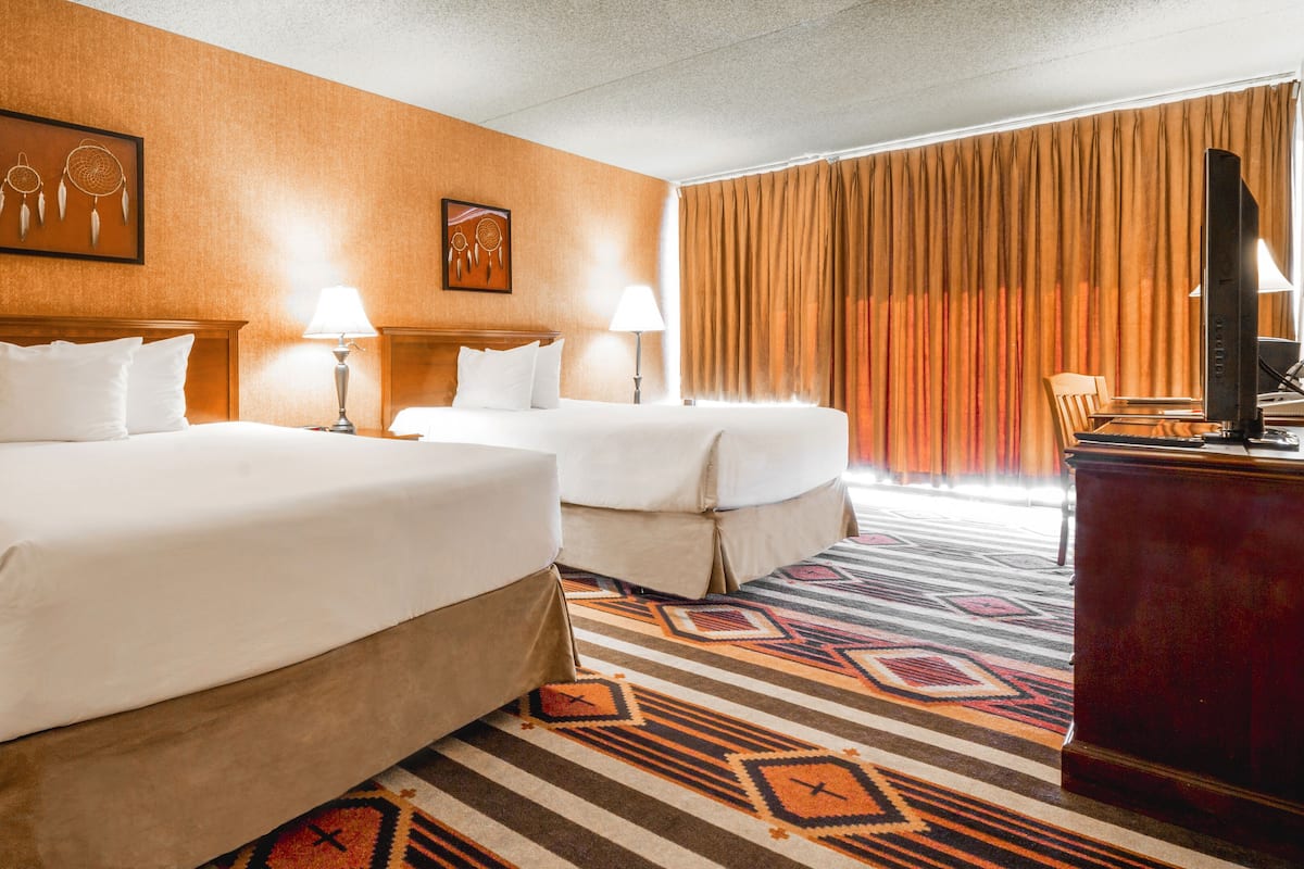 Habitación de hotel con dos camas, un escritorio, un televisor y una alfombra estampada.