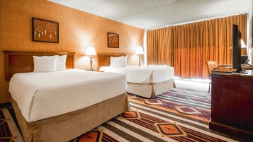 A hotel room with two beds, a desk, a TV, and a patterned carpet.