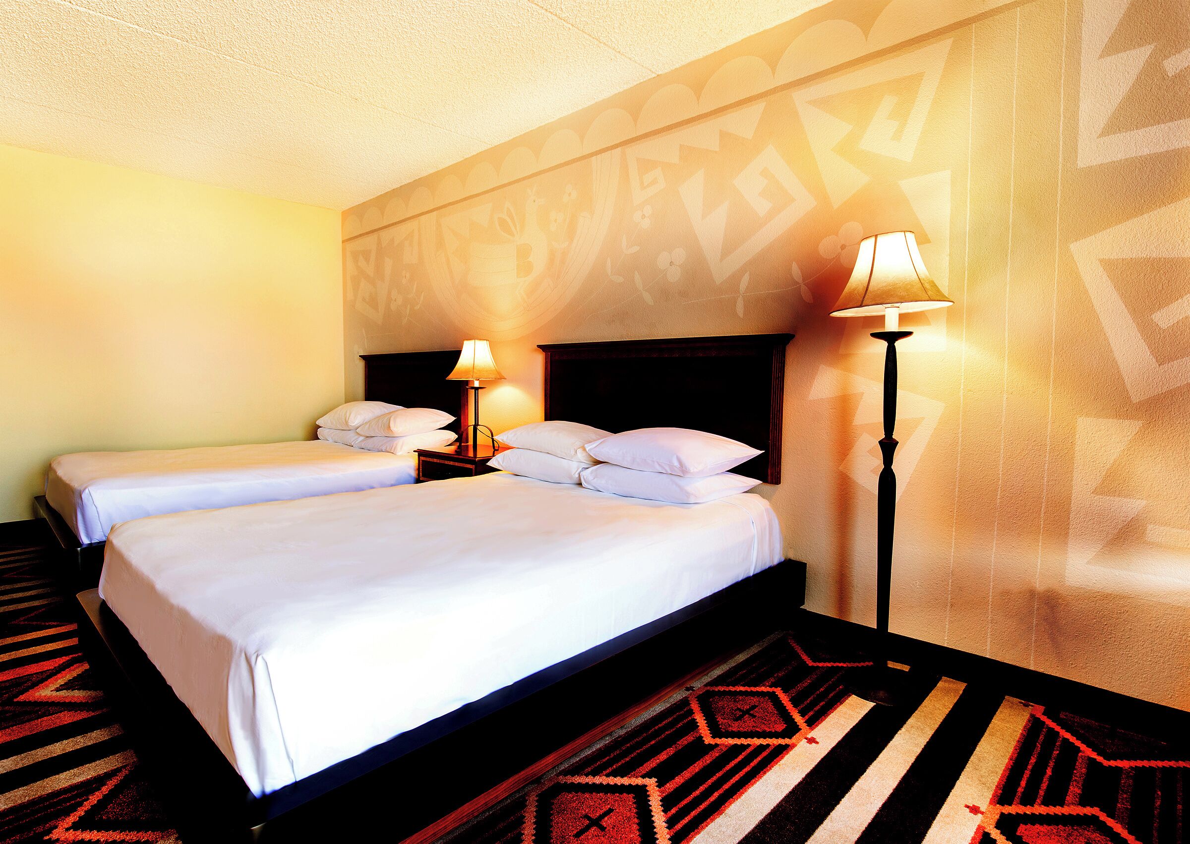 Een hotelkamer met twee bedden, een nachtkastje, een lamp en een kamer met behang.