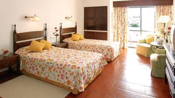 A hotel room with two beds, a sitting area, and a view of the outside.